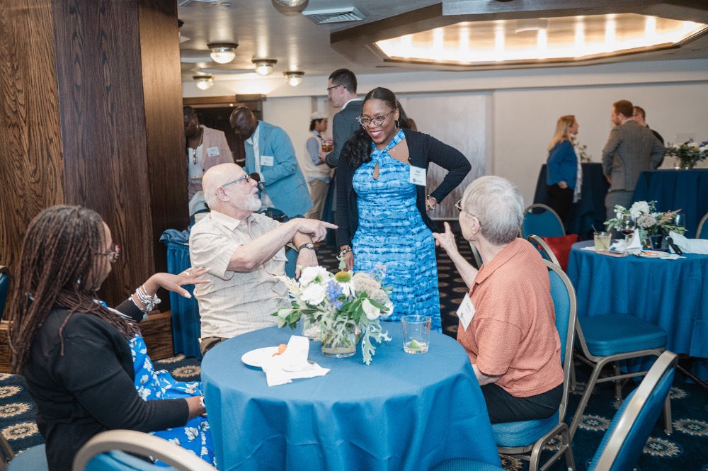 3 people point to woman while she is standing and smiling at them